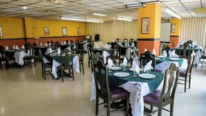 Un amplio comedor con varias mesas dispuestas para el servicio, con manteles verdes y servilletas blancas.
