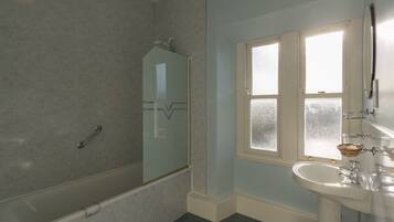 A bathroom with a bathtub, a glass-enclosed shower, a sink with a mirror, and a window.