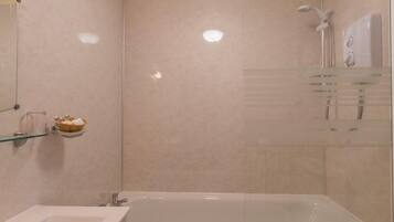 A modern bathroom with a glass-enclosed shower, a large bathtub, and a glass shelf with toiletries.