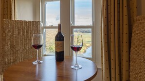 A table with a bottle of wine and two glasses, set against a window with a view of a landscape. - Lutwidge Arms Limited (Holmrook)