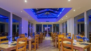 A modern dining area with wooden tables and chairs, a glass ceiling, and large windows. - Lutwidge Arms Limited (Holmrook)