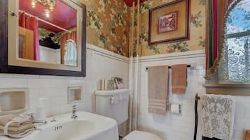 A bathroom with a white sink, mirror, and toilet. There are floral wallpaper and a framed picture on the wall.
