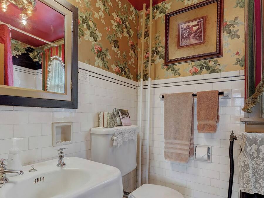 A bathroom with a white sink, mirror, and toilet. There are floral wallpaper and a framed picture on the wall.