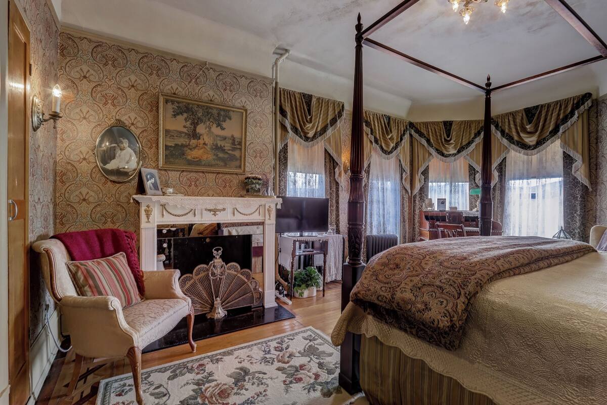 Un dormitorio con cama con dosel, chimenea, televisor y comedor con mesa y sillas.