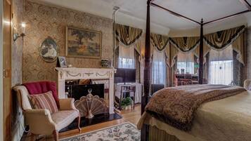 A bedroom with a four-poster bed, a fireplace, a television, and a dining area with a table and chairs.