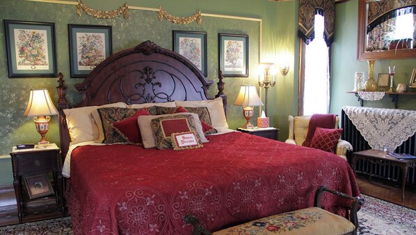 Un dormitorio tradicional con una cama grande, dos mesitas de noche con lámparas, una silla y un aparador.