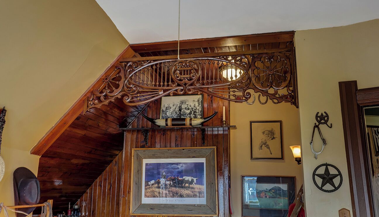 A room with a wooden staircase, a framed picture of a cowboy scene, a wall-mounted light fixture, and a star-shaped decoration.