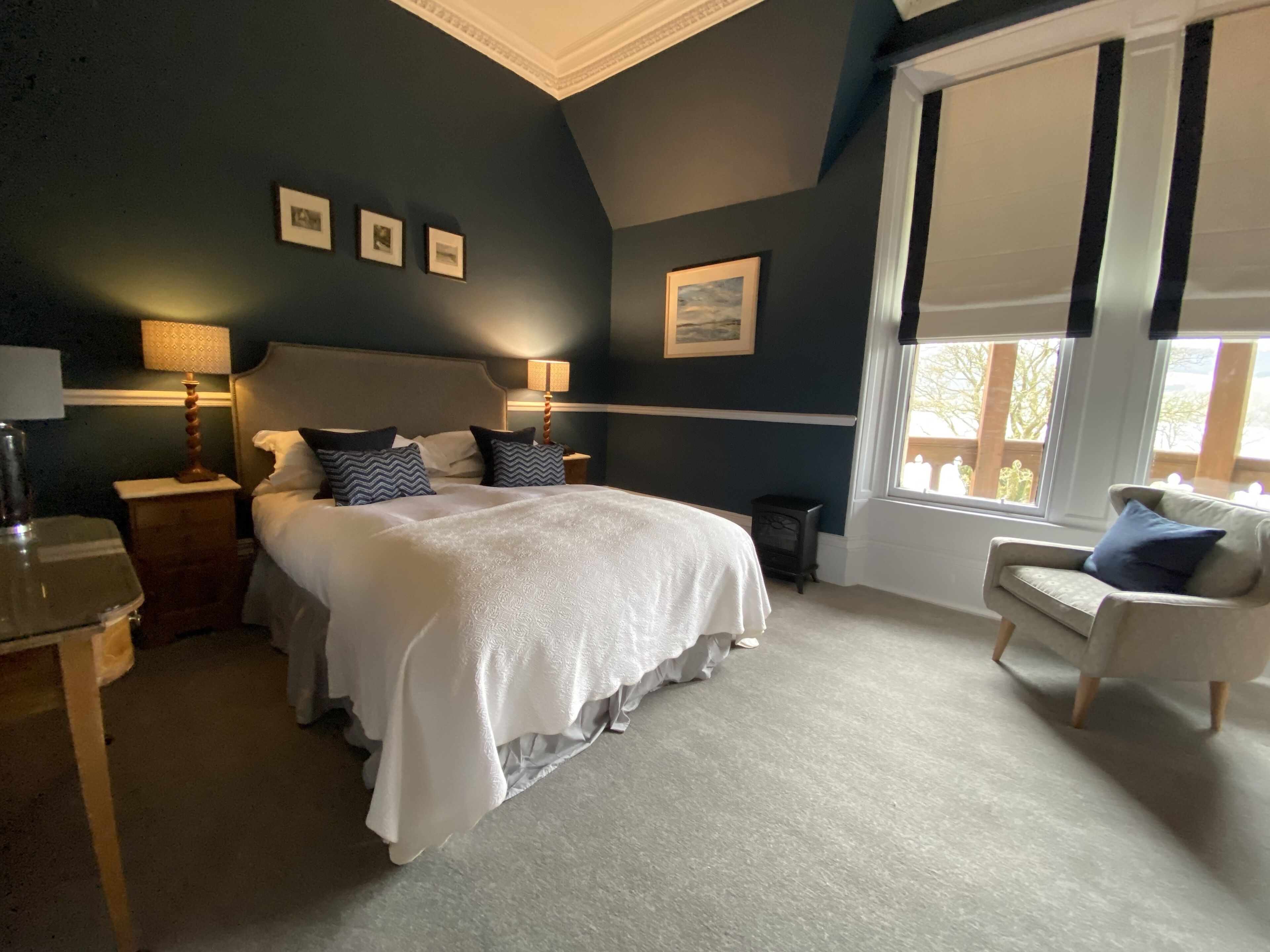 A bedroom with a large bed, a nightstand, a lamp, a chair, and a window with blinds.