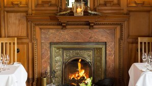 A dining room with a fireplace, wooden paneling, and tables set for dining.