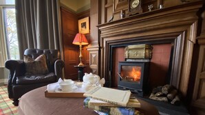 A cozy room with a fireplace, a leather armchair, a table with books and a teapot, and a window with curtains.
