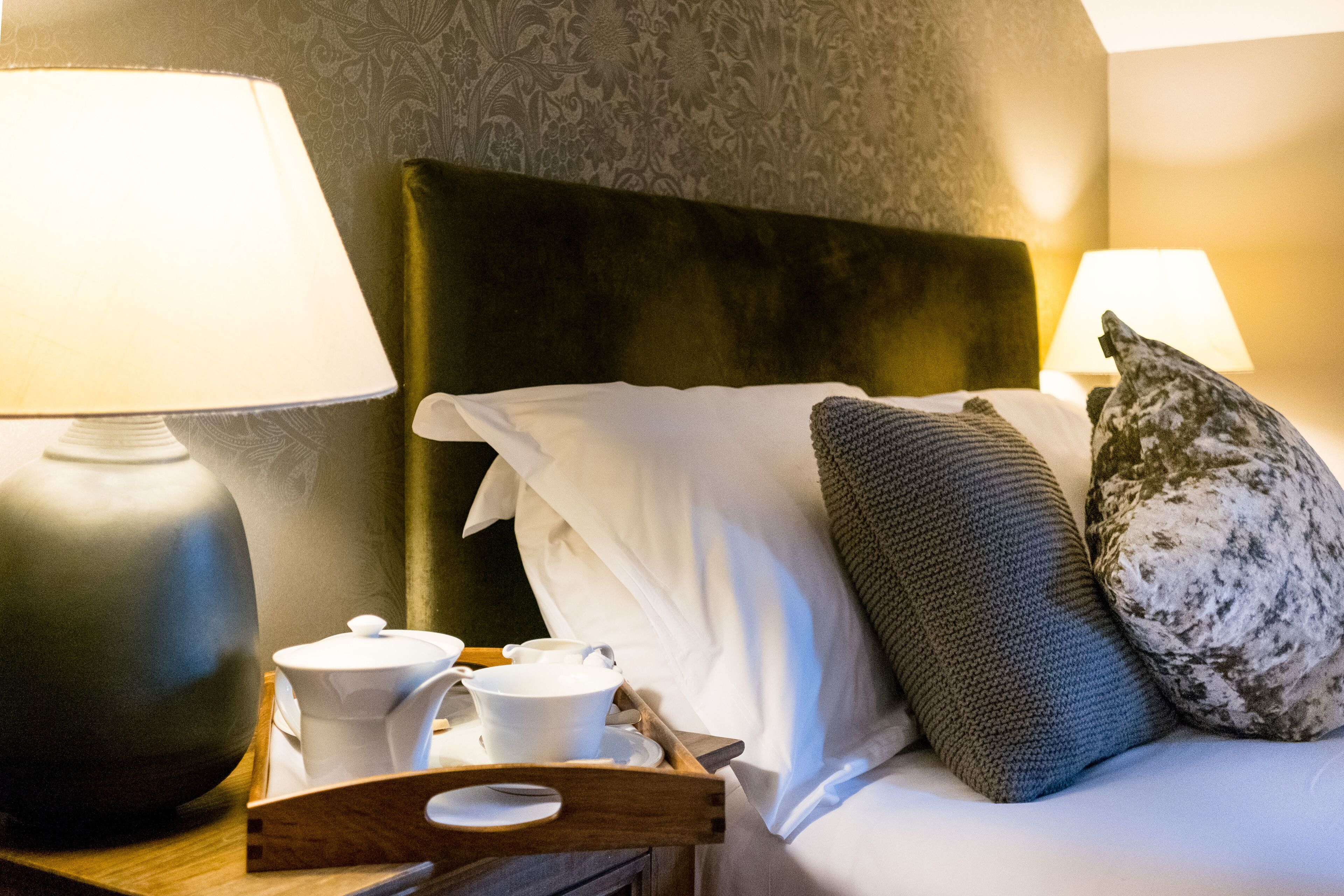 A neatly made bed with a green headboard, white pillows, and a tray with a teapot and cups.