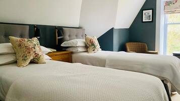 A hotel room with two beds, a nightstand, a chair, and a window with a view.