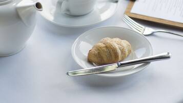 Uma mesa posta para refeição, com um bule, xícaras, um prato com um croissant e um cardápio.