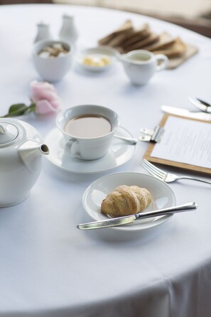 A table set for a meal with a teapot, cups, a plate with a croissant, and a menu. - Knockderry Country House Hotel (Helensburgh)