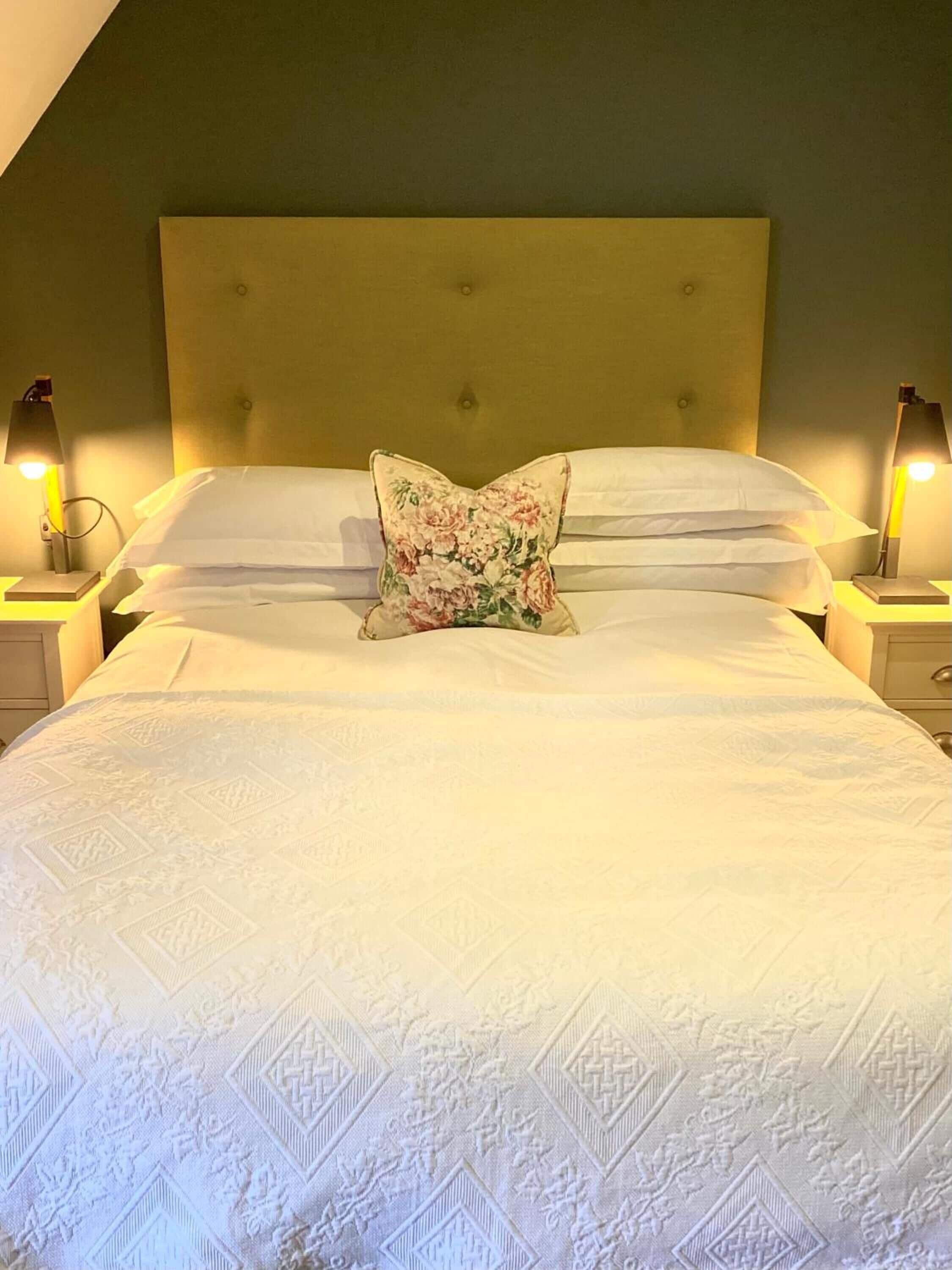 Een net opgemaakt bed met een sierkussen, twee bedlampen en een hoofdbord.