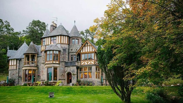 A large, historic stone building with multiple towers and a well-maintained lawn.