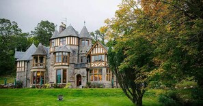 Un grand bâtiment historique en pierre, doté de nombreuses tours et d’une pelouse bien entretenue.