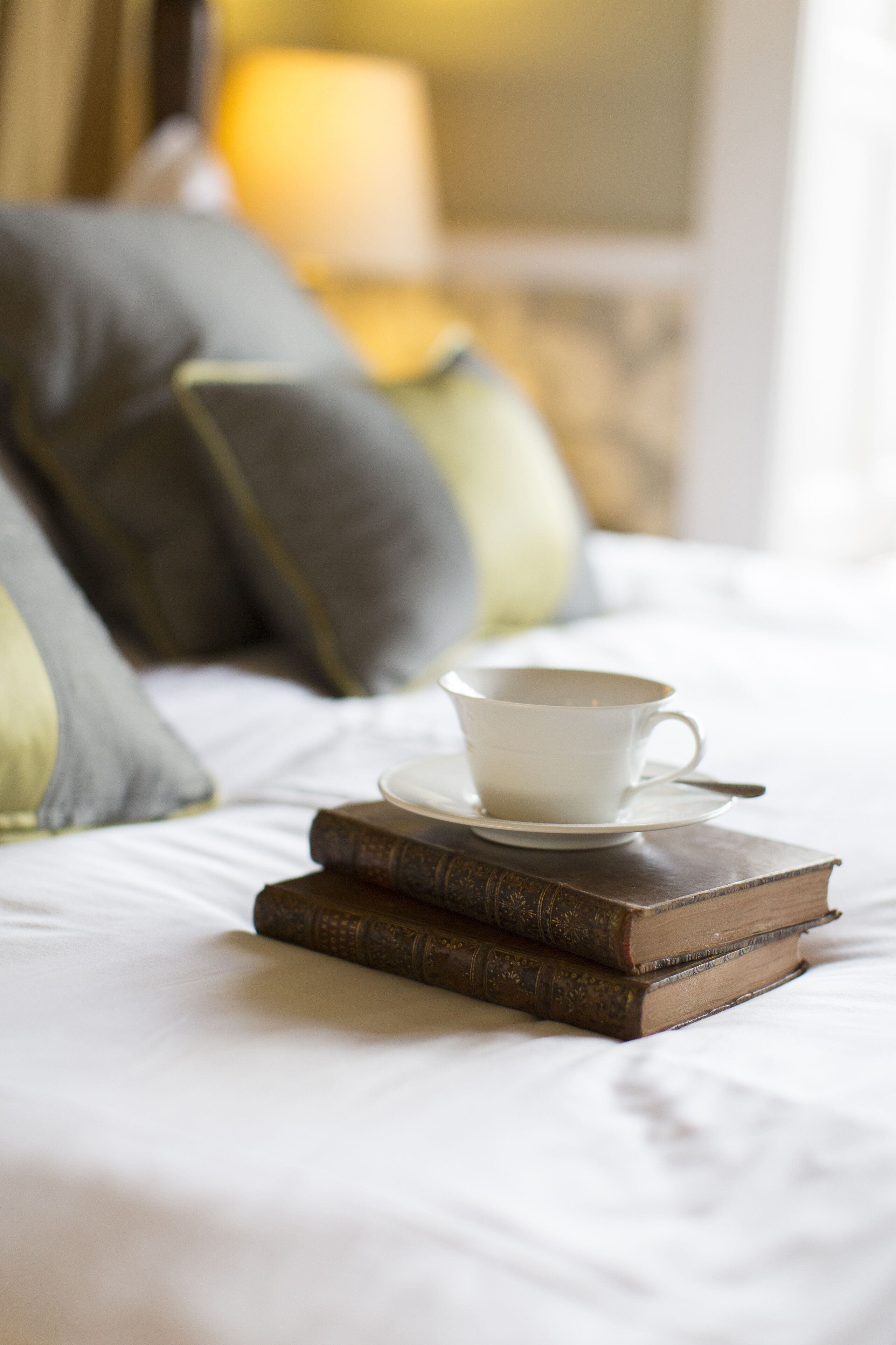 A bed with a cup and saucer, two books, and pillows.