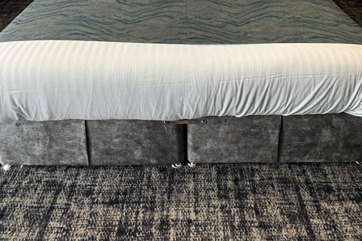 A hotel room with a large bed, grey headboard, and a textured carpet.