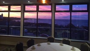 Comedor con una mesa dispuesta para seis personas, ventanas amplias con vistas al mar y al paisaje urbano, y una lámpara colgante moderna.