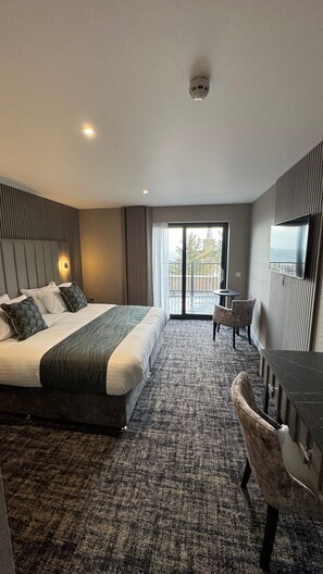 A modern hotel room with a large bed, a desk, and a view of a building through the window. - The Knowes Hotel & Restaurant (Macduff)
