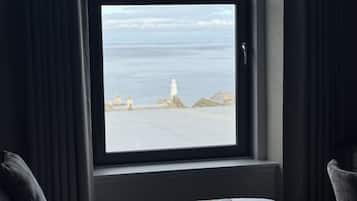 Habitación de hotel con un amplio ventanal que ofrece vistas al mar y un faro.