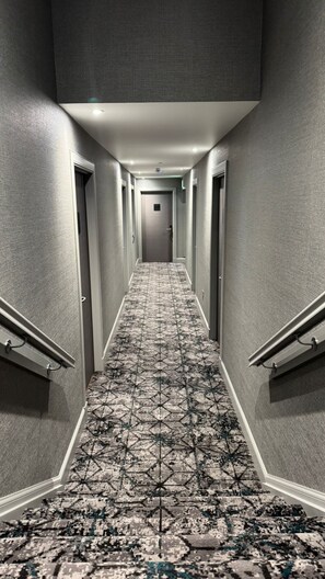 A long, narrow hallway with a patterned carpet, grey walls, and doors on both sides. - The Knowes Hotel & Restaurant (Macduff)