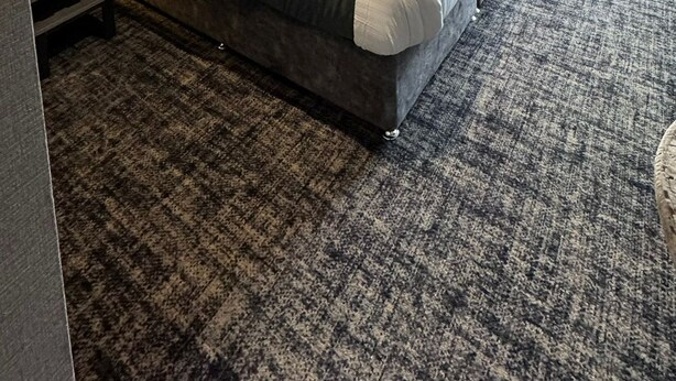 Una habitación de hotel moderna con una cama grande, un cabecero con líneas verticales, una mesita de noche, una lámpara fijada a la pared y vistas amplias por una ventana grande.