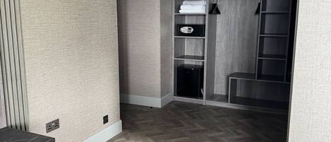 Een hotelkamer met een houten vloer in een herringbone patroon, een inbouwkast met spiegel, en een klein zitgedeelte met een donker vloerkleed.