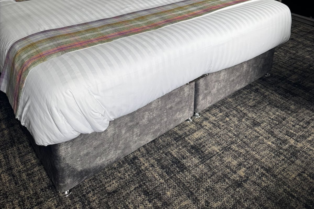 A hotel room with a large bed, a bedside table, a mirror, and a door.