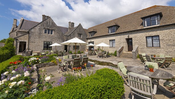 A stone building with outdoor seating and a garden. - Mortons Manor (Wareham)