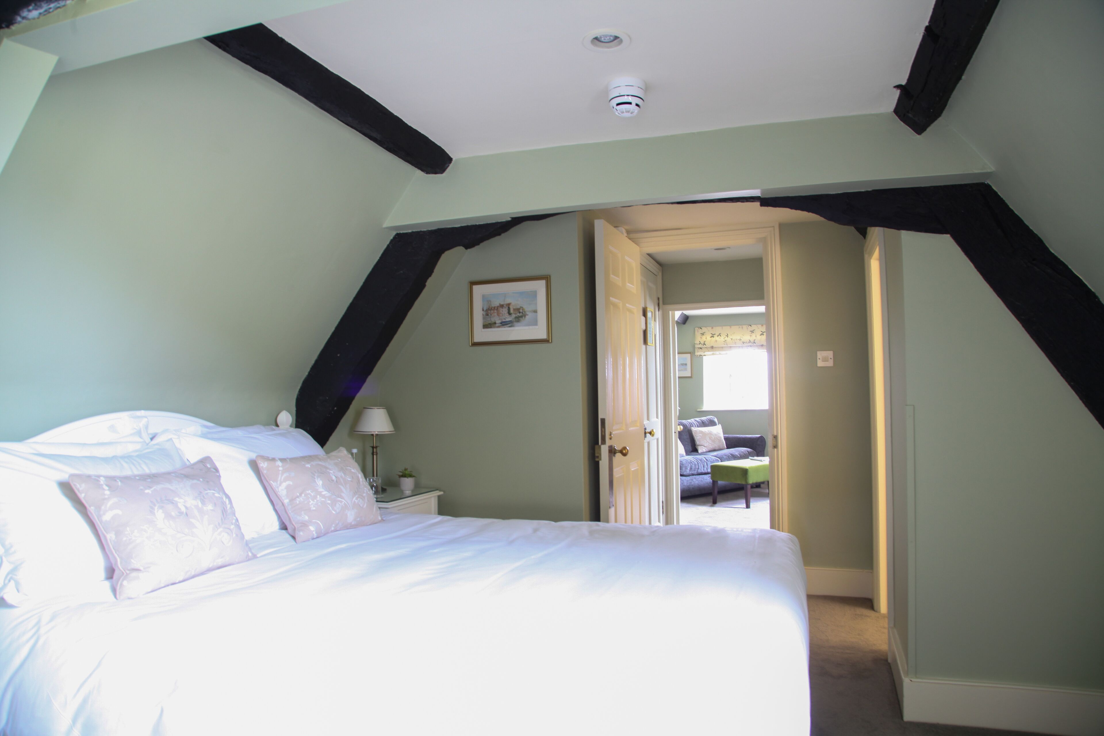 A bedroom with a large bed, a nightstand, a lamp, and a door leading to another room.