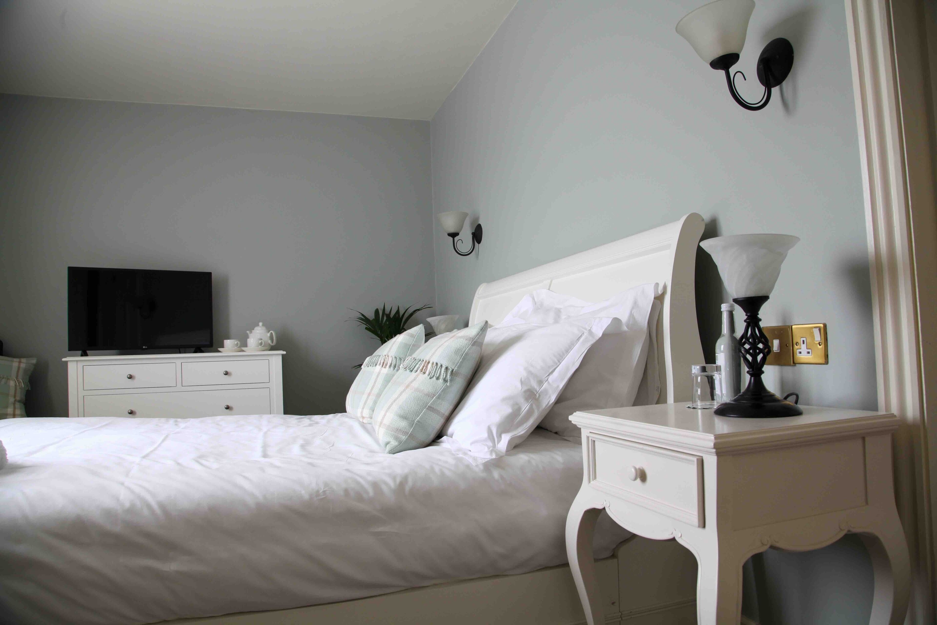 Ein Schlafzimmer mit einem Bett, einem Nachttisch, einer Lampe, einem Fernseher und Wandleuchten.
