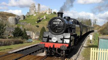 A steam locomotive numbered 80078 on tracks with a historic stone castle in the background.