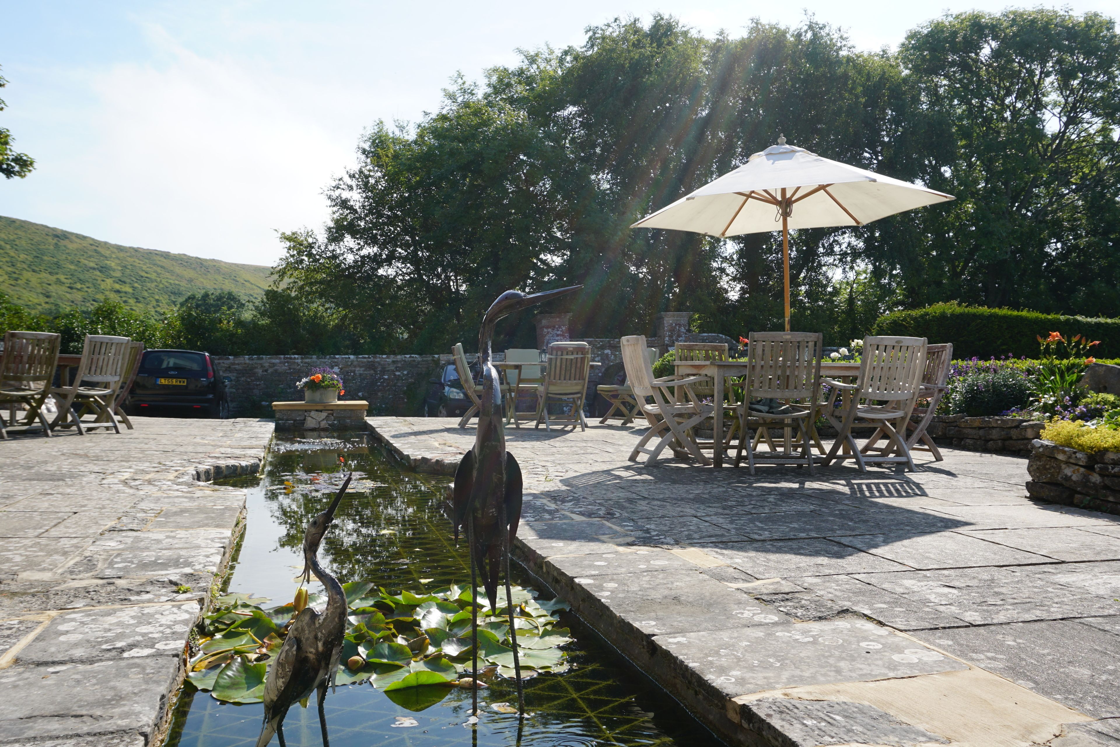 A patio with a pond, chairs, and an umbrella.