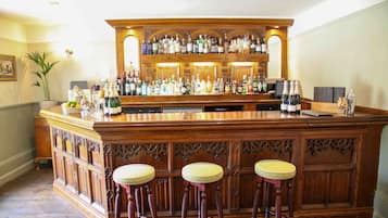 A bar area with a wooden bar counter, multiple stools, and a variety of bottles and glasses.