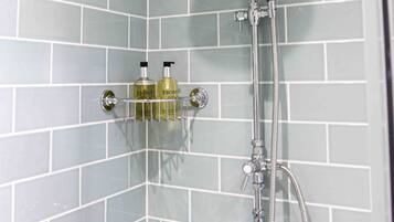 A shower with a handheld showerhead and a wall-mounted faucet. There are two bottles of lotion on a shelf below the shower.