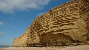A coastal cliff with layered rock formations and a sandy beach. - Mortons Manor (Wareham)