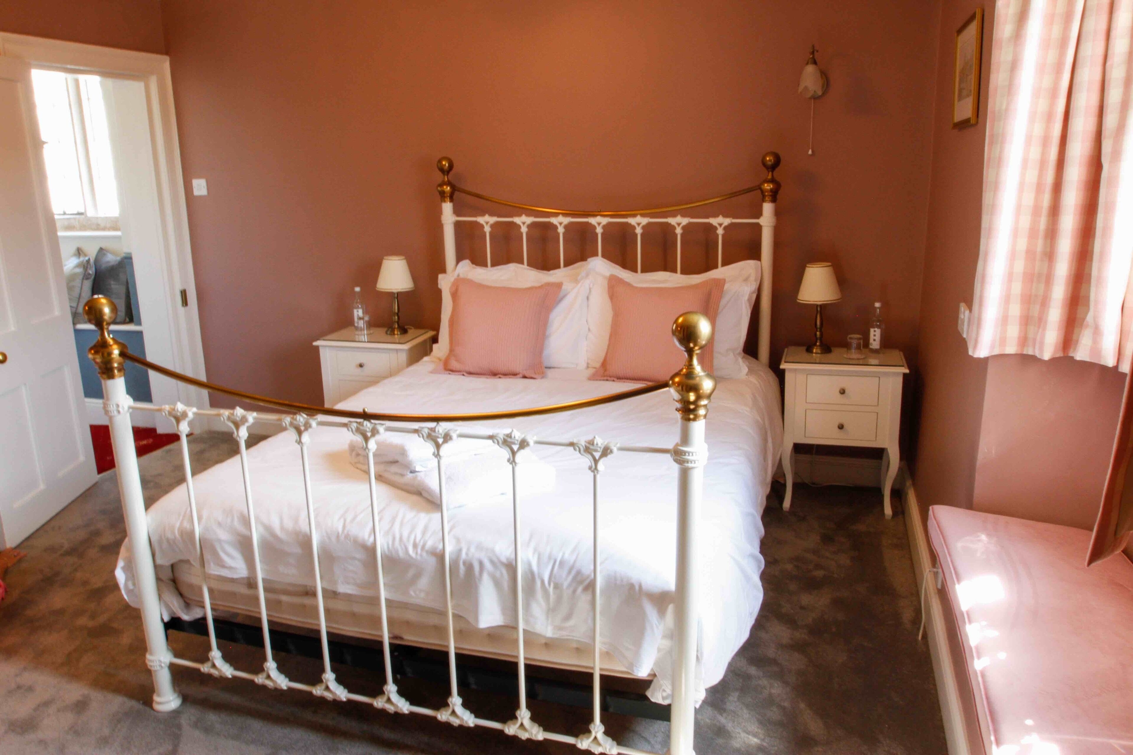 A bedroom with a white metal bed frame, two bedside tables with lamps, and a pink curtain.
