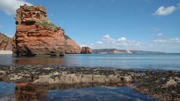 A coastal landscape with a prominent rock formation and calm sea.