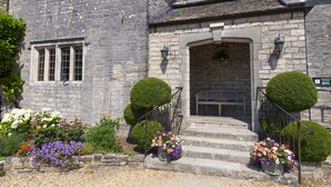 A stone building with a stone staircase, a bench, and flower arrangements. - Mortons Manor (Wareham)