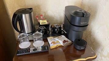 A coffee station with a coffee maker, espresso machine, kettle, cups, and coffee pods on a wooden table.