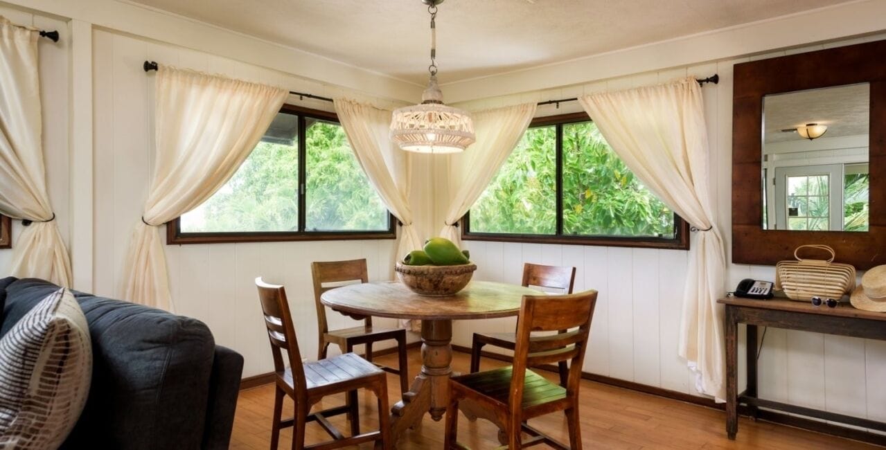 A dining area with a round table, wooden chairs, a chandelier, and a window with curtains.