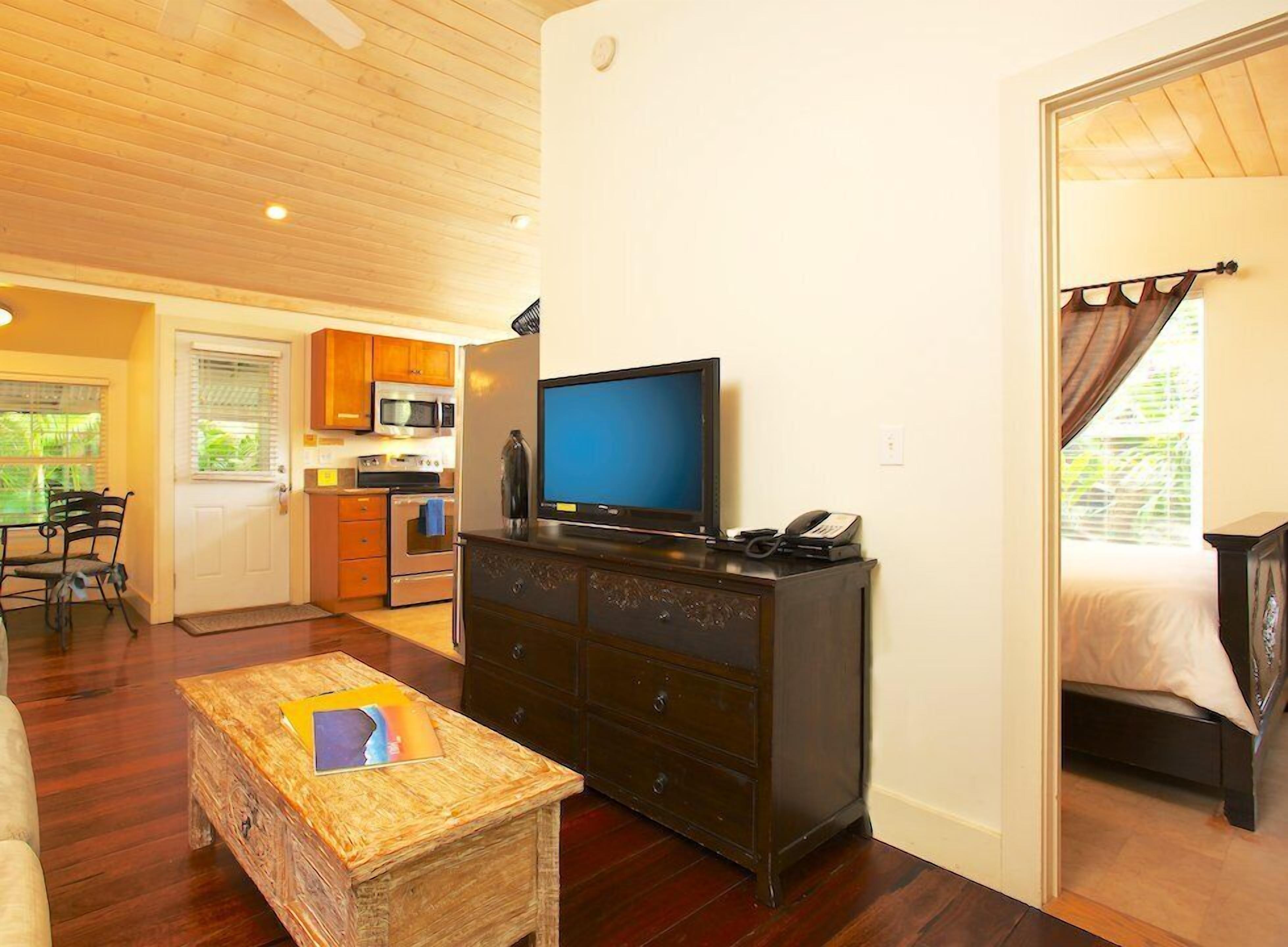 Un espacio habitable compacto con kitchenette, televisor, cómoda y cama.