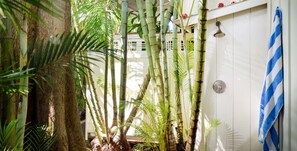 A bathroom with bamboo plants, a shower, and a blue and white striped towel hanging on the wall.