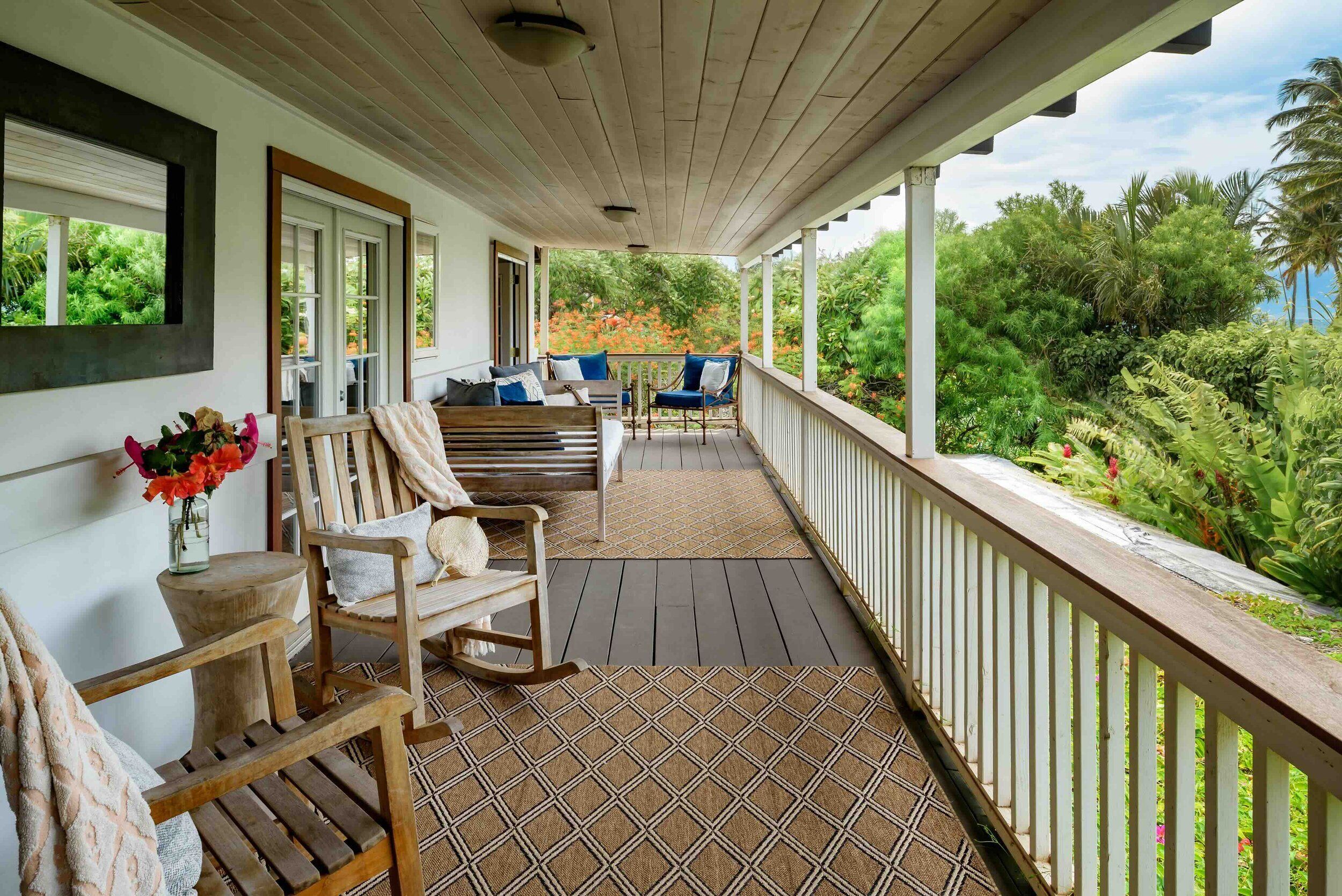 A covered porch with wooden furniture, a patterned rug, and a view of lush greenery.