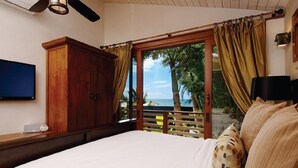 A bedroom with a large bed, wooden wardrobe, and a view of the ocean through a sliding door. - Paia Inn (Paia)