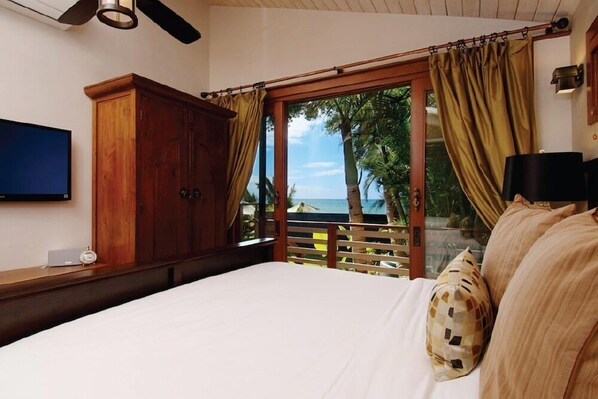 Un dormitorio con una cama grande, un armario de madera y vistas al océano a través de un puertas correderas.