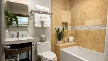 A bathroom with a sink, toilet, and bathtub. There are towels and a plant on the counter.