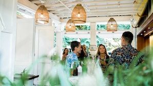 A dining area with a long table, wicker hanging lamps, and a view of greenery outside. - Paia Inn (Paia)